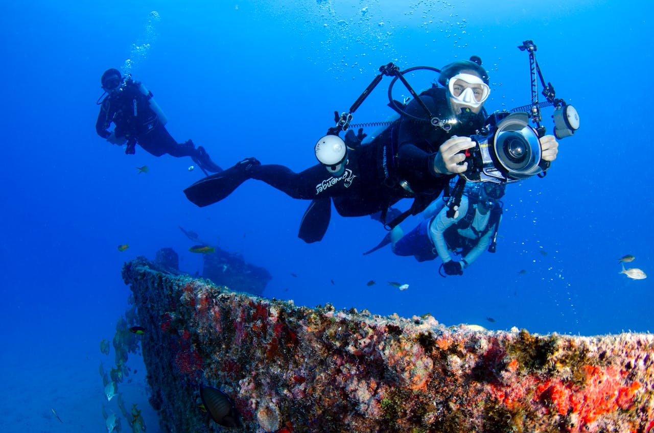 Two scuba divers capturing the vibrant marine life near an underwater wreck in crystal clear waters.